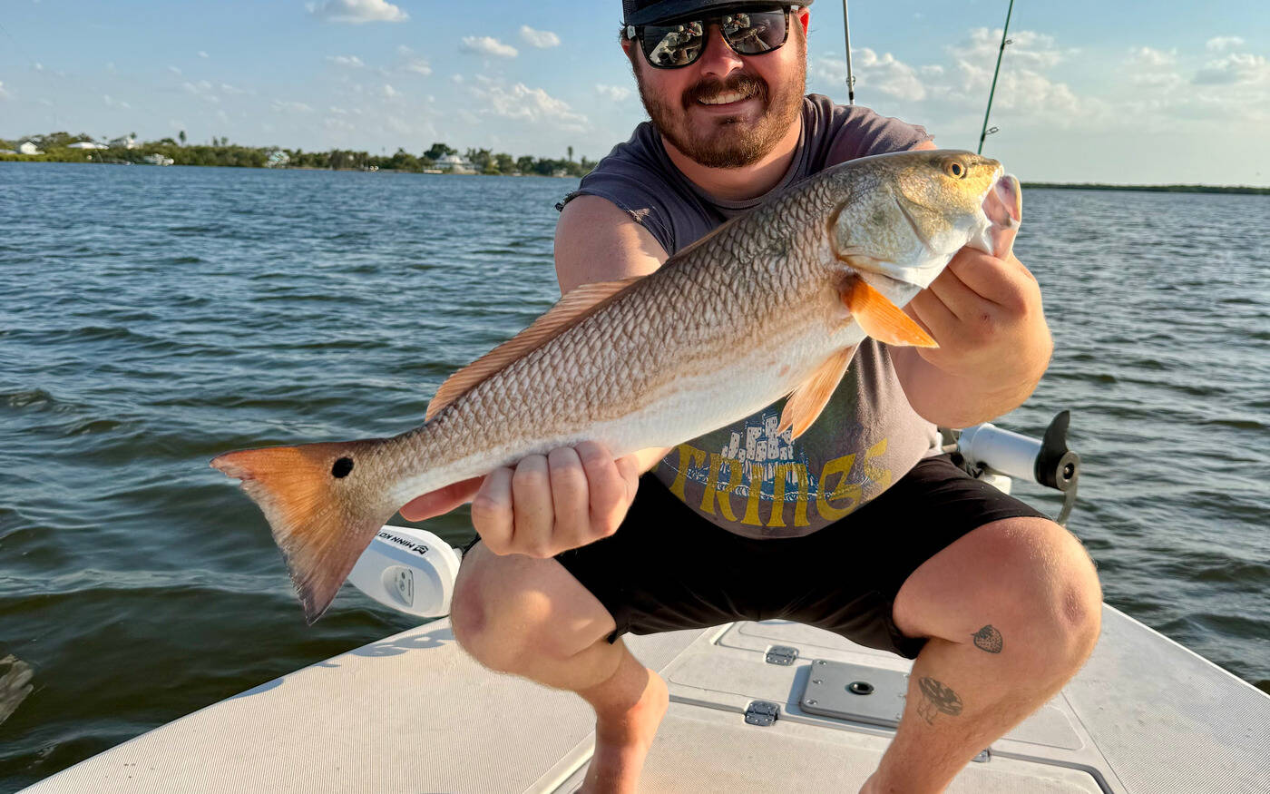 Angler on a flats boat holding a copper-colored redfish, the black spot near its tail clearly visible