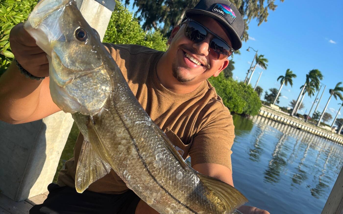 Angler at a Florida dock in golden-hour light holding a snook, its black lateral line running the length of the fish