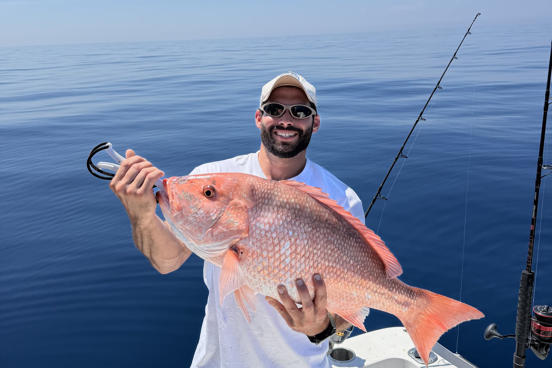 Angler holding an American red snapper above a boat deck on calm blue water