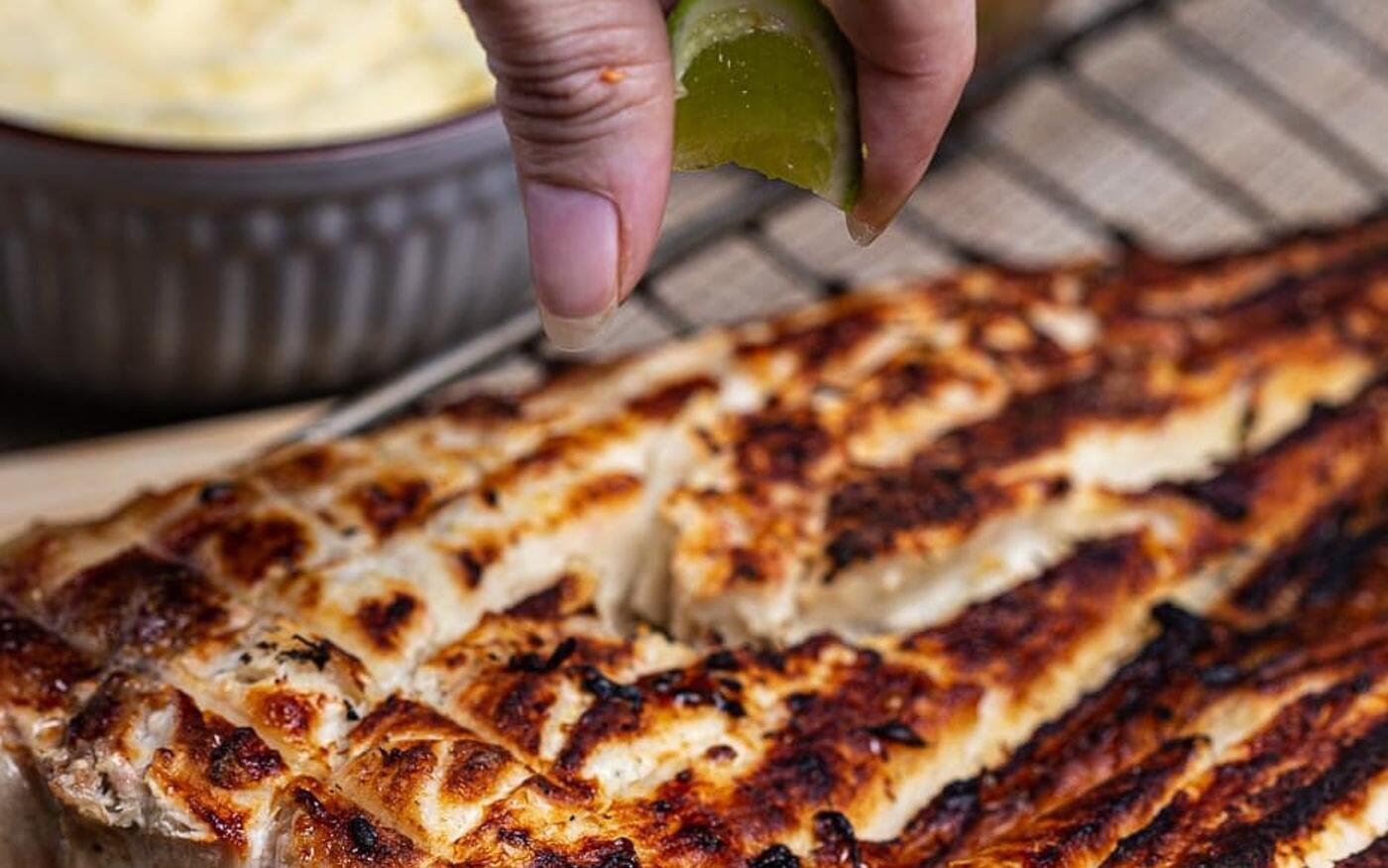 A hand squeezing fresh lime over fish fillets sizzling on a grill