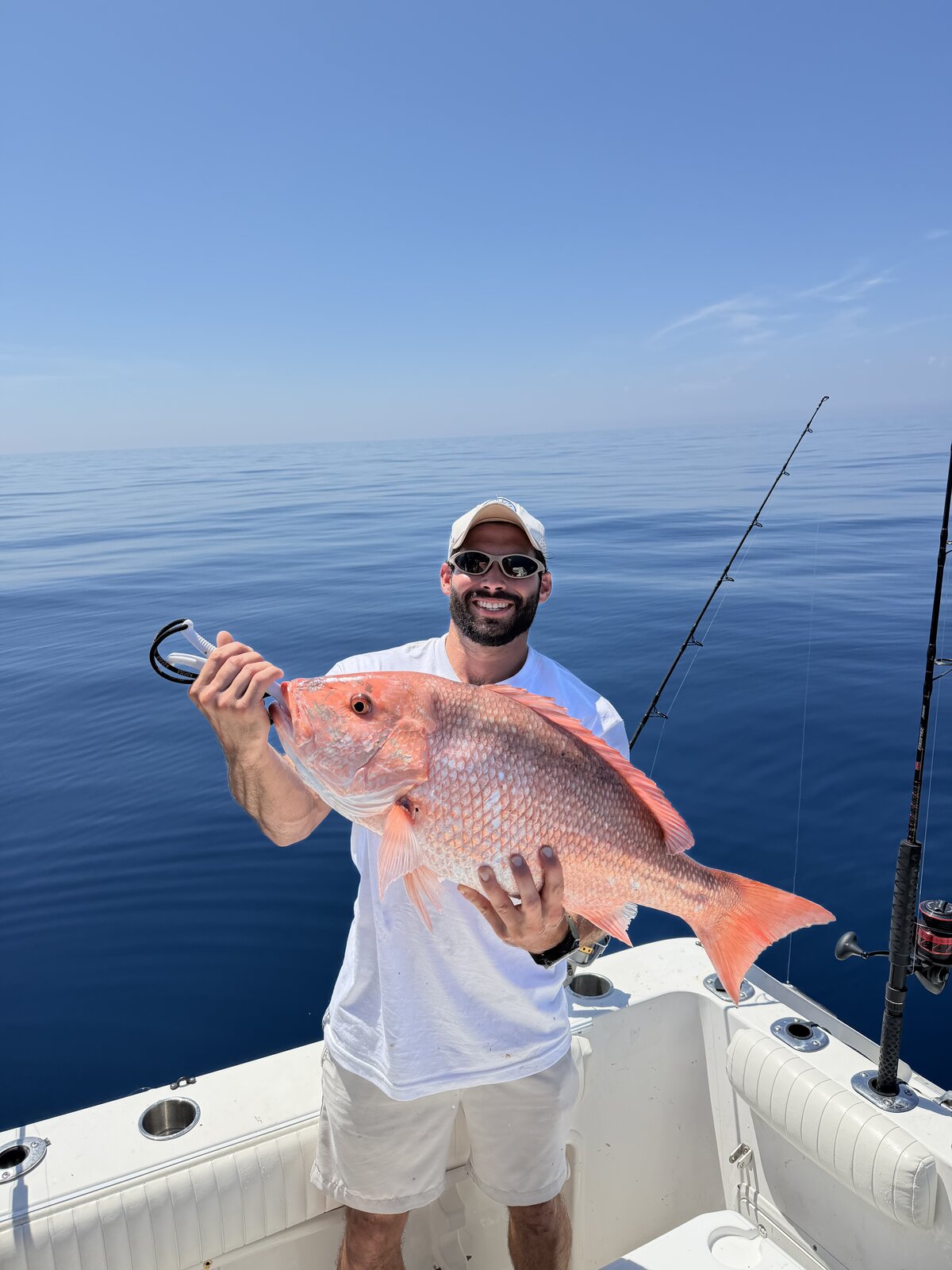 Angler holding an American red snapper broadside above the deck of a boat on calm blue water