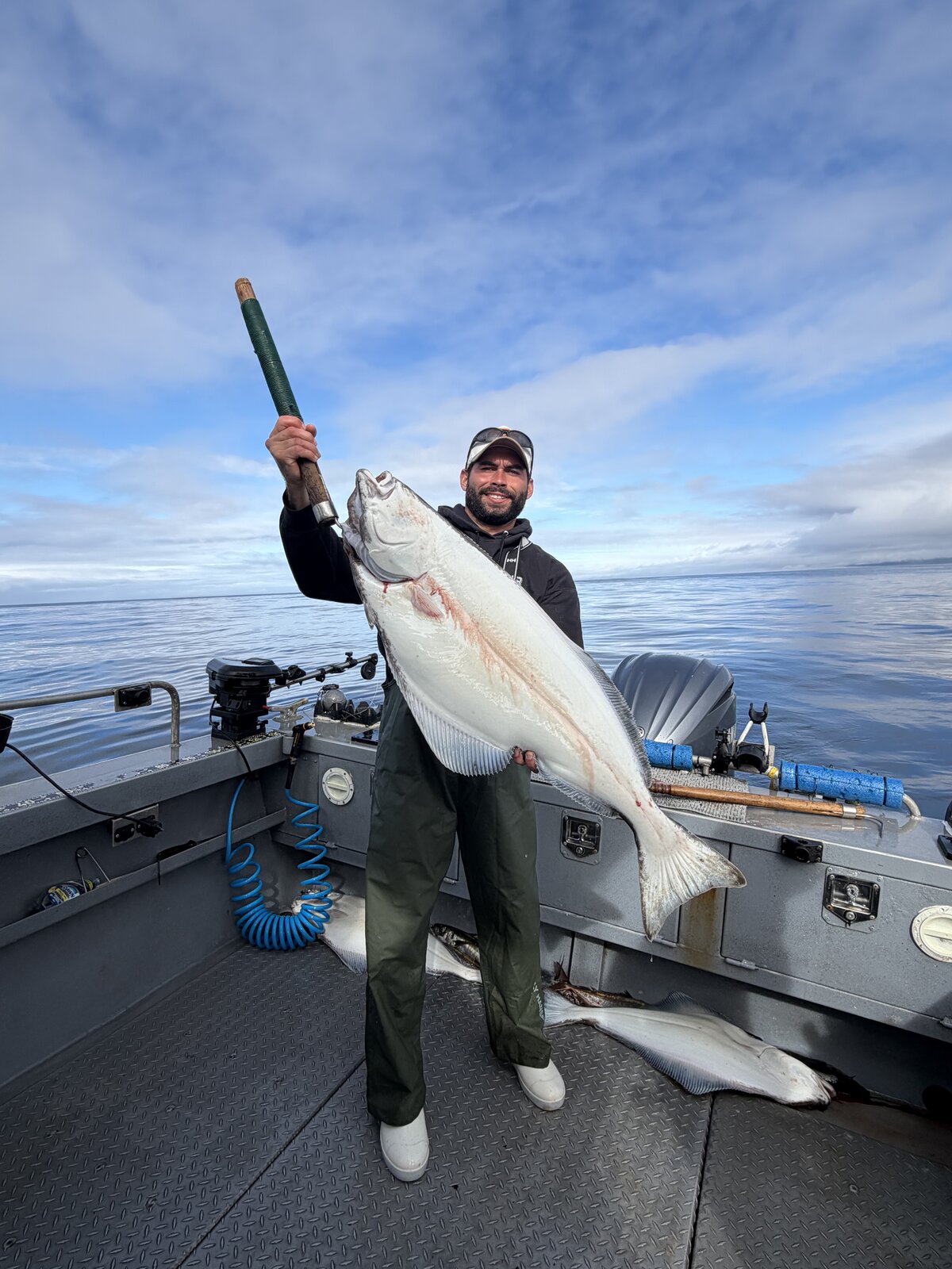Angler aboard a boat holding a Pacific halibut with its pale underside facing the camera